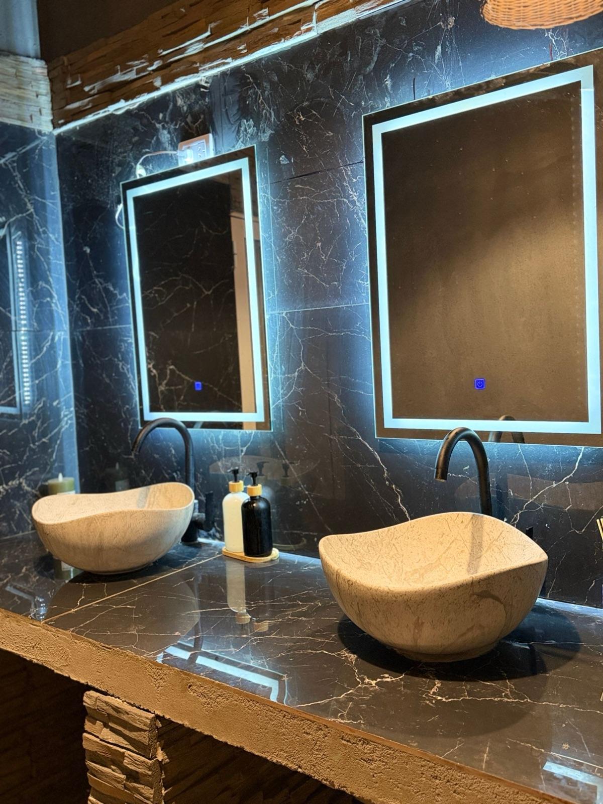 Baño de hombres: bachas de piedra y espejos con luz
