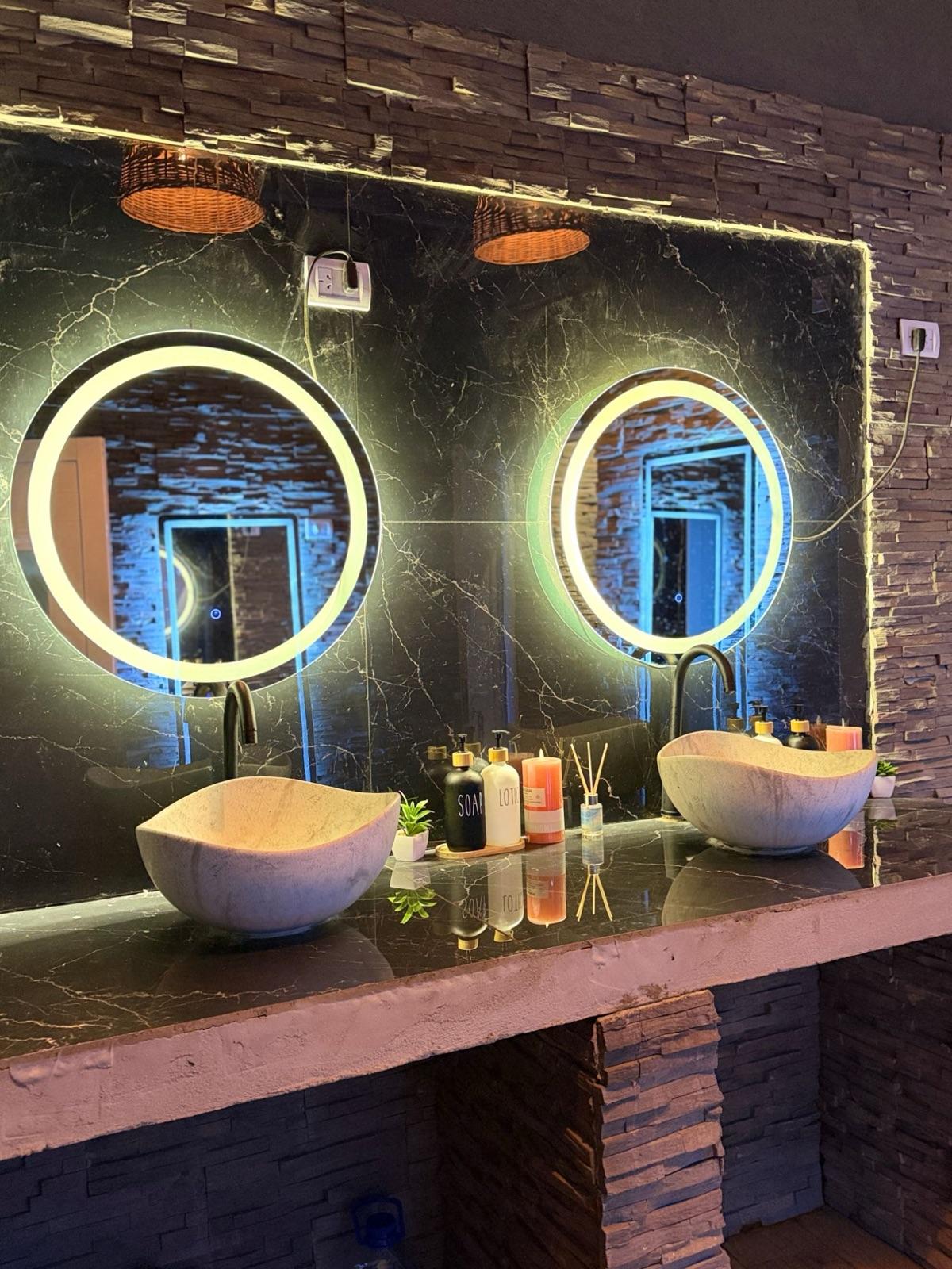 Baño de mujeres: mesada de mármol negro con espejos redondos iluminados