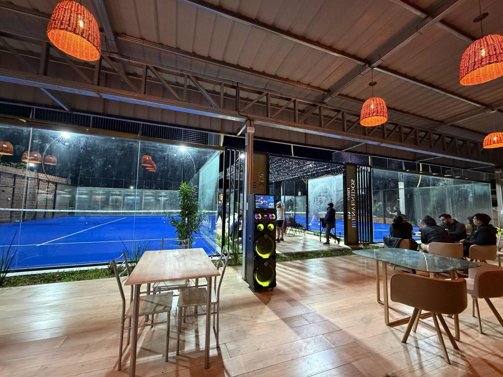 Zona de mesas techada con lámparas de mimbre y vista a las dos canchas